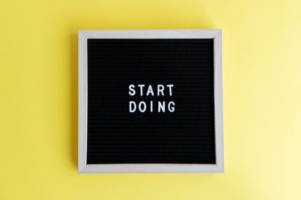 Black message board with 'Start Doing' on a bright yellow background for inspiration.